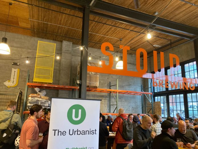 Stoup Capitol Hill Urbanist Meetup An Urbanist banner standing in a corner of a brewery with a few dozen people gathered chatting.