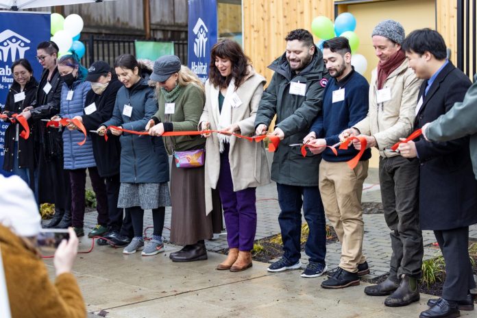 Eleven people hold a ribbon outside a housing project.