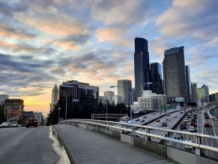 I-5 with sunset and Seattle skyline by Doug Trumm 20240223 I-5 and the Seattle Skyline at sunset looking down Yesler Way to Elliott Bay with Smith Tower peeking out on the left and the car-clogged I-5 trench on the right.