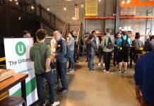 Join The Urbanist for Our Monthly Meetup on July 25th An Urbanist banner standing in a corner of a brewery with a few dozen people gathered chatting.