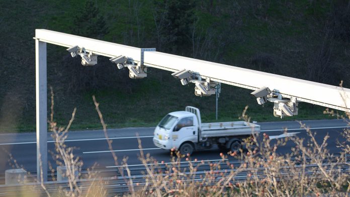 A photo shows a row of plate reader cameras over a highway with a truck going by.