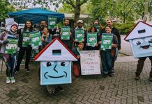 Seattle Social Housing Staffs Up, Nets $115 Million A group of about 20 advocates pose with signs next to House-y the social housing mascot
