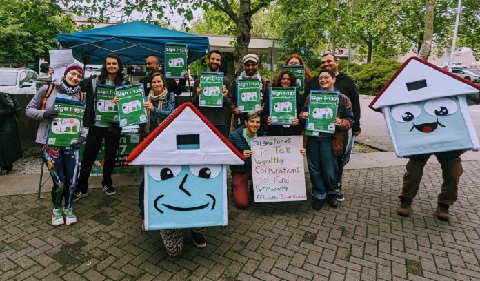 Folklife-Friday-House-Our-Neighbors-1280p A group of about 20 advocates pose with signs next to House-y the social housing mascot
