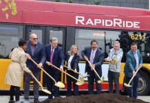 J Line Breaks Ground, Delivering Bus and Bike Upgrades by 2027 Officials stand in front of a red RapidRide bus with golden shovels with a scoop of ceremonial dirt.