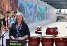 Claudia Balducci Wants to Tackle King County’s Challenges Head-On as Executive Claudia Balducci stands at a lectern with drums next to her and drummers dressed in traditional Japanese garb behind.