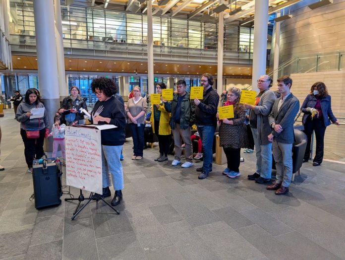 Shemona and Housing Advocates at Seattel City Hall - Trumm 20241113 A sign reads Resilient communities on the lectern in the lobby of city hall and people stand behind the speaker holding signs saying a protest JumpStart commitments and invest on Seattle's future.
