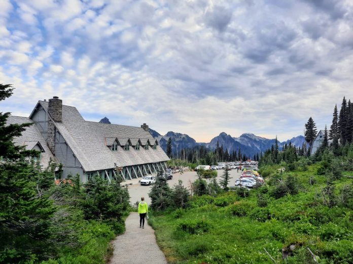 Paradise Inn Lodge at Mount Rainier National Park - Trumm 20240821 A women walks down the trail to Paradise Inn and the crowded parking lot adjoining it. A mountain ridge and cirrus clouds are on the horizon.