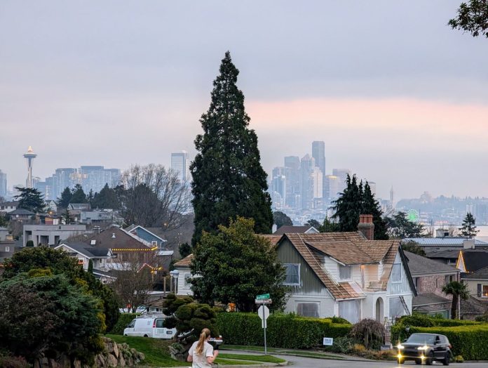 Seattle Skyline from Wallingford with Lake Union - Trumm 20241203 A woman jogs down Wallingford Avenue on a block of single family homes with Lake Union and the Seattle skyline in the background.