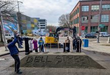 Seattle Breaks Ground on Bell Street Bike Lane, Waterfront Park Linkage Bell Street is written into the pile of sand that was used in the ceremonial groundbreaking shoveling. A man hoists his child and officials mill about after the ceremony.