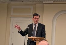 Op-Ed: We Need a Bolder Bob Ferguson as Governor Ferguson wears a dark suit and stands at a lectern gesturing with his right hand.