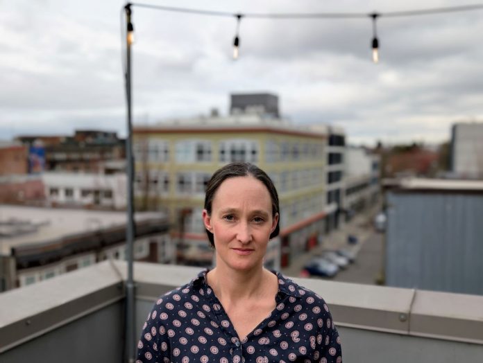 Katie Wilson Portrait - Doug Trumm 20250310 Wilson stands on a rooftop in Capitol Hill with a Mona Lisa smile. She's a White middle-aged woman with dark hair.