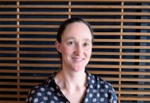 Katie Wilson Jumps In Seattle Mayor Race as Progressive Coalition-Builder Katie wears a blue patterned blouse and stands in front of a wood slatted wall.
