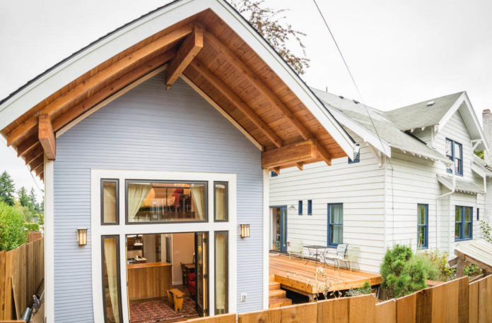 ADU stock photo A small cottage with its doors open, revealing living room, behind a larger parent house