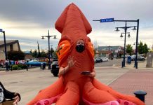 Op-Ed: Will Bremerton Build Its First Protected Bike Lane? A woman in an octopus costume stands nexts to bollards at a 6th avenue intersection and gestures and reads a story to kids. Cars zip through the intersection.