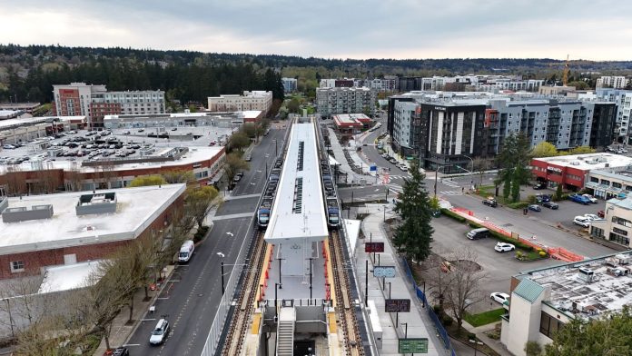 APR25-Trains-at-Downtown-Redmond-Station-0485 Villeneuve A elevated platform sits on the side of an urban road with a smattering of large midrise apartment buildings bordering it.