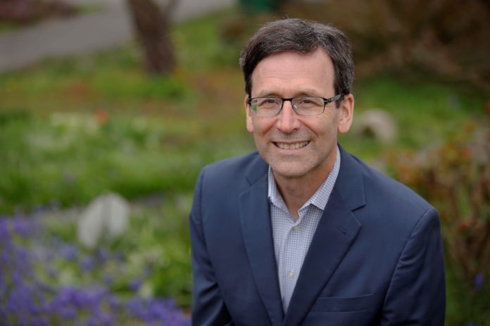 Ferguson is a middle aged White man in glasses in a suit posing by some flowers