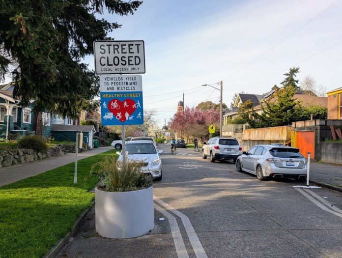 A concrete planter narrow the crossing distance at an intersection with a sign saying "Street closed, local access only, Stay Healthy Street."