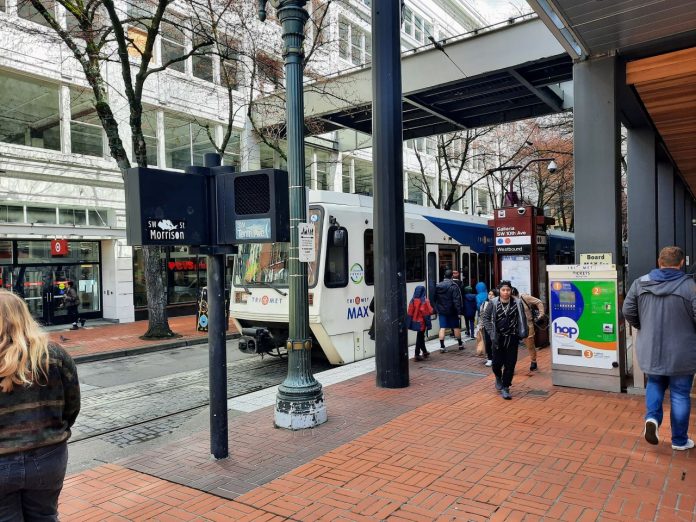 A handful of passenger wait or deboard a MAX light rail train on Morrison Street in Downtown Portland.