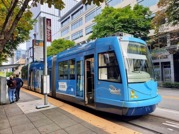 South Lake Union Streetcar on Westlake Ave - Trumm 20231014 A blue streetcar at a stop along Westlake Avenue with three passengers on the platform.