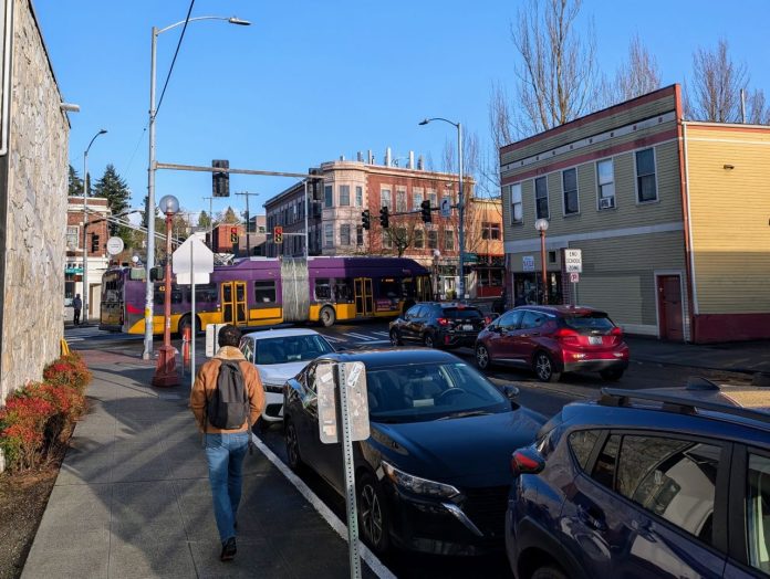 A bus on Rainier Avenue passes by as a pedestrian walks up the side street in Columbia City.