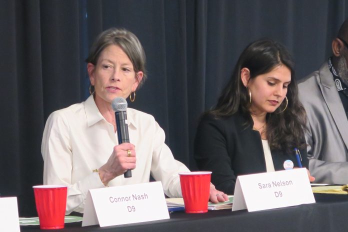 Nelson and Rinck SCC forum SaraNelson.PhotoCreditClaraCantor Sara Nelson holds a microphone and wears a white button-up shirts. She sits a long table next to Alexis Rinck, who wears a black blazer and hoop earrings.
