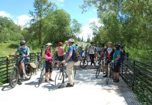 Join The Urbanist for Campaign Events Ahead of the November Election A group of over dozen people with their bikes on a wetland boardwalk segment of the trail.
