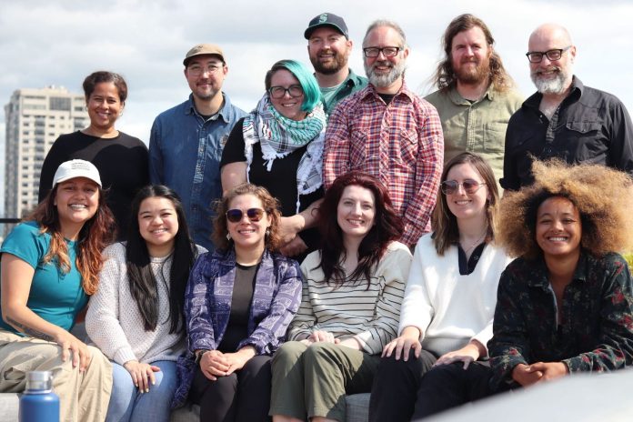 2025 Urbanist Elections Committee via Hannah Sabio Howell The group stands on a rooftop with the Seattle skyline and Elliott Bay in the background.