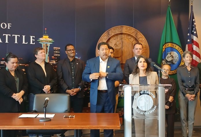 Rinck stands at the lectern and a group of supporters stands behind her, including colleagues Rob Saka and Sara Nelson and Mayor Bruce Harrell.