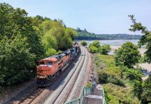 Op-Ed: PCC Provides Model for State Rail Ownership in Washington State A BNSF freight train heads north along the Puget Sound coast, passing under the pedestrian bridge at Carkeek Park. A tree-covered ridge is on the left.