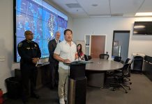 Harrell Pushes to Expand Recently Passed Surveillance Camera Pilot Program Mayor Bruce Harrell stands at a lectern flanked by Police Chief Shon Barnes and Councilmember Bob Kettle, who chairs the Public Safety Committee. A projection screen displays surveillance footage.