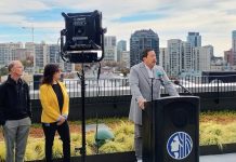 Harrell Issues Conditional Support Letter for County’s Capitol Hill Crisis Center Harrell stands at a lectern with the Seattle City Seal and the skyline visible behind him from a midrise rooftop.