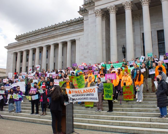 Olympia Lobby Day at Capitol Steps Credit_ Isabel Lay More than 100 advocates hold signs urging a balanced tax code on the steps of the state Capitol building with its many marble columns.