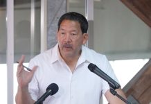 In Last Stand, Harrell Intensifies Negative Attacks on Wilson Wearing a white polo Harrell stands at a lectern gesturing with a pen in his hand.