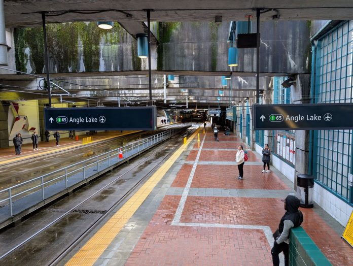 A view of the platform at International District Station from partway up the escalator. A few dozens passengers are waiting for trains.