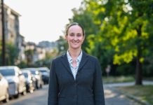 Op-Ed: Katie Wilson Can Be Seattle’s Climate Mayor for Renters Wilson wears a blzer and stands on an urban street with trees and a line of parked cars in the background.
