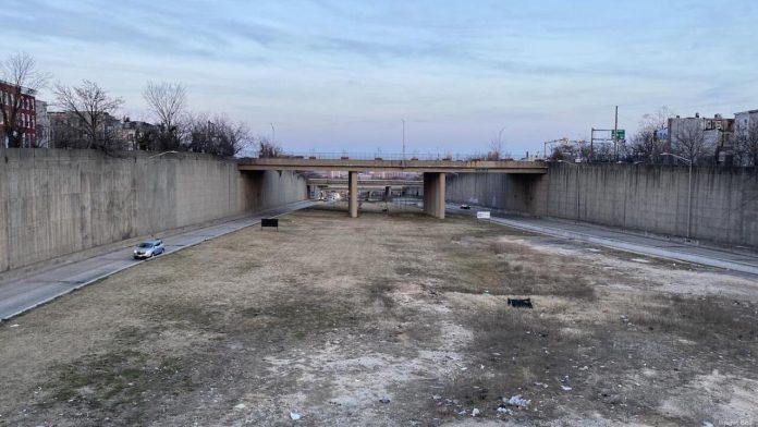 A barren trenched has an access road on the city but empty field down the middle with bridges spanning the trench to connect the street grid.
