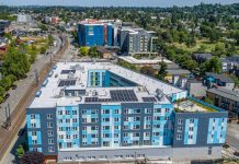 Affordable Housing Expands in Seattle, Especially in the Rainier Valley An aerial view of a six-story light blue building with a central court and the light rail line just to the west.