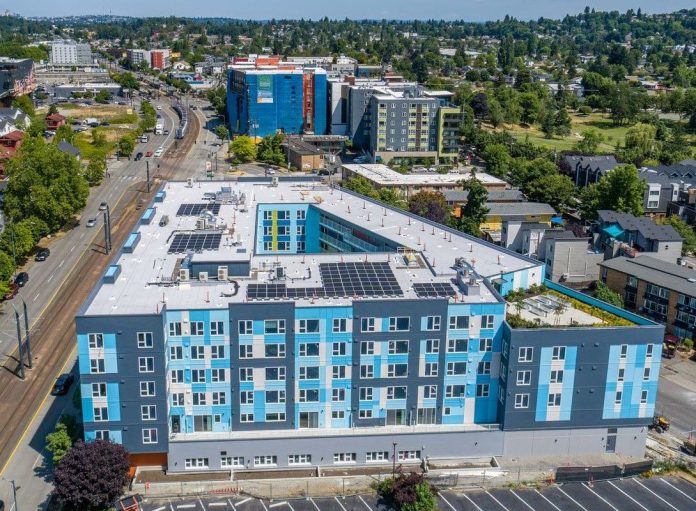 An aerial view of a six-story light blue building with a central court and the light rail line just to the west.