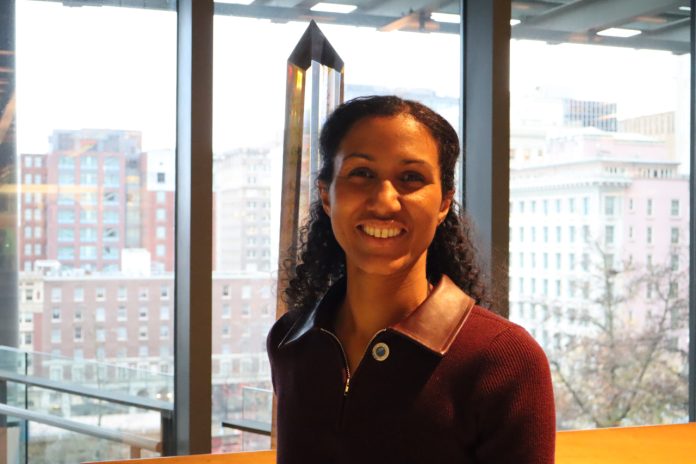 Foster smiles and stands in the atrium of Council Chambers with the south downtown skyline in the background.