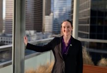 One Week In, Katie Wilson Charts the Path Ahead Wilson wears a black blazer and stands on the balcony outside her seventh floor office, with the downtown skyline in the background