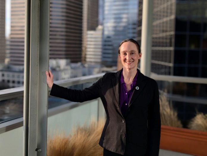 Katie Wilson on City Hall balcony with Seattle Skyline crop - Trumm _20260107 Wilson wears a black blazer and stands on the balcony outside her seventh floor office, with the downtown skyline in the background