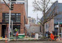 Wilson Promotes Sam Steele to Lead Seattle Permitting Department A half dozen hard-hatted construction workers work at a site between two midrise buildings on Ballard's Market Street.