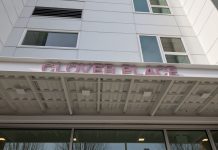 Supportive Housing Building Opens Near Seattle’s Woodland Park The metal awning includes the building name in red letters. The building has a white facade.