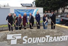 Sound Transit Breaks Ground on Stride S3 Bothell-to-Shoreline Bus Line Eight Sound Transit leaders lift a shovelful of ceremonial dirt next to an agency logo and poster board