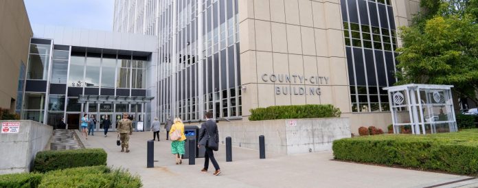 A stream of people in formal clothes walk into a modern concrete and plate class courthouse building